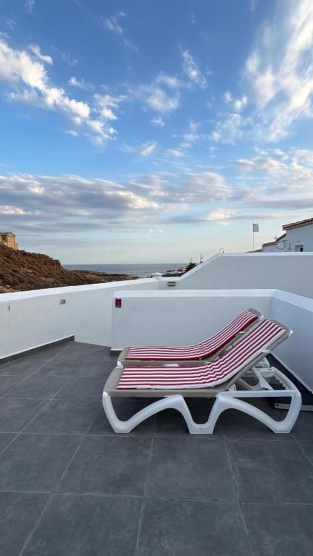 Terraza privada con vistas al mar. Disfruta del sol en las cómodas tumbonas a rayas mientras contemplas el océano Atlántico. Tu espacio perfecto para relajarte y disfrutar del paraíso costero.